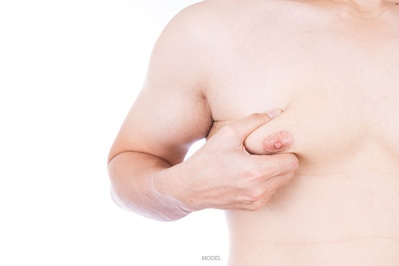 Close-up image of a man pinching his fatty breast skin (man boob)